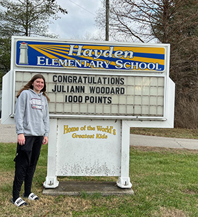 Juliann Woodard in front of Hayden Elementary School sign that congratulates her for receiving 1,000 points