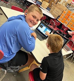 Older student turning around to smile next to a younger student