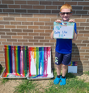 School boy outside holding up his artwork