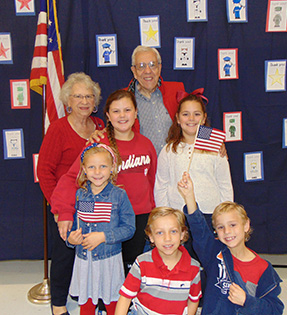 Two older adults with five children and American flags in front of a blue background