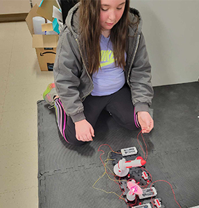 School girl on the classroom floor working on a robot