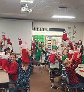 Students in classroom holding up Christmas stockings