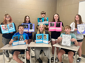 Group of students holding up their book reports in the classroom