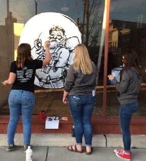 3 students painting on a window