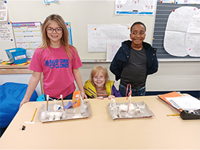 Three students posing for a picture next their projects