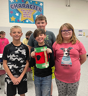 four students and one is holding a green and red craft