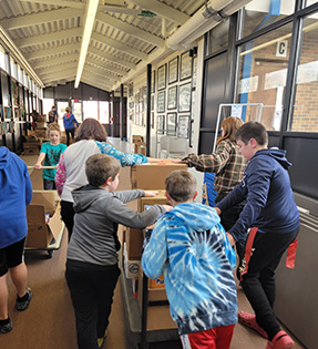 3 students and staff moving boxes down a hallway on hand trucks